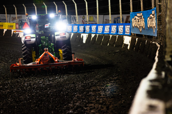 A tractor uses an implement to prepare the racing surface of a dirt track. 